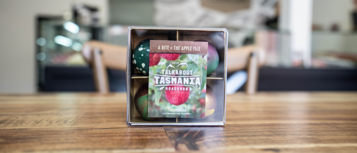 A clear plastic box containing chocolates. The label on the box reads: 'A BITE OF THE APPLE ISLE. TALKABOUT TASMANIA ROADSHOW'