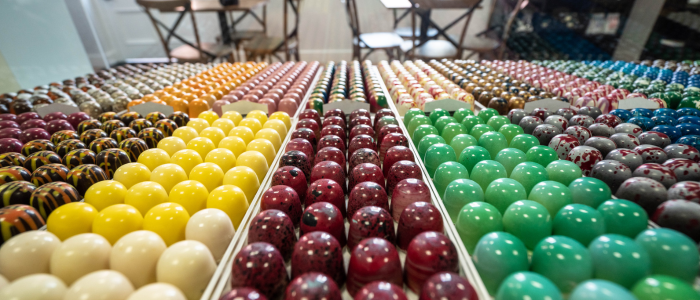 A display of colorful, round objects arranged in rows and columns. The objects appear to be various types of candies or chocolates, each with different colors and patterns. The display is organized into sections with each section containing a specific color or pattern of the candies/chocolates.